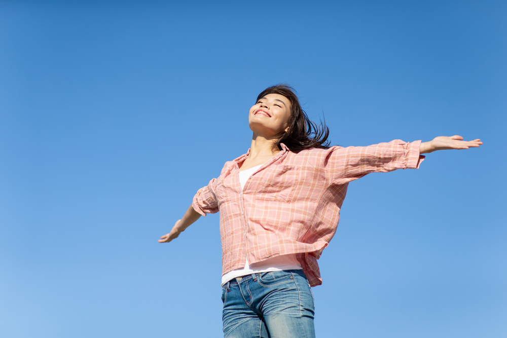 Asian,Young,Woman,Cheering,Open,Arms,With,Isolated,Sky,Blue